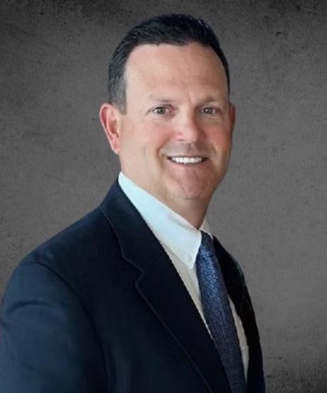 Smiling man in a dark suit and tie against a gray studio backdrop