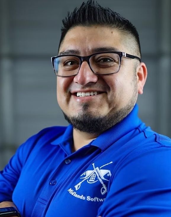 Smiling person in glasses wearing a bright blue polo shirt with a logo, against a blurred gray background