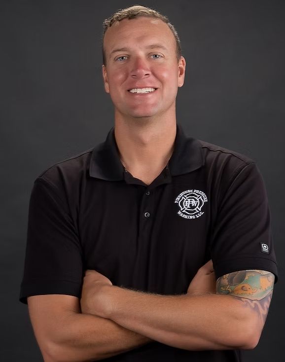 Smiling person in a black polo shirt with arms crossed against a dark gray background