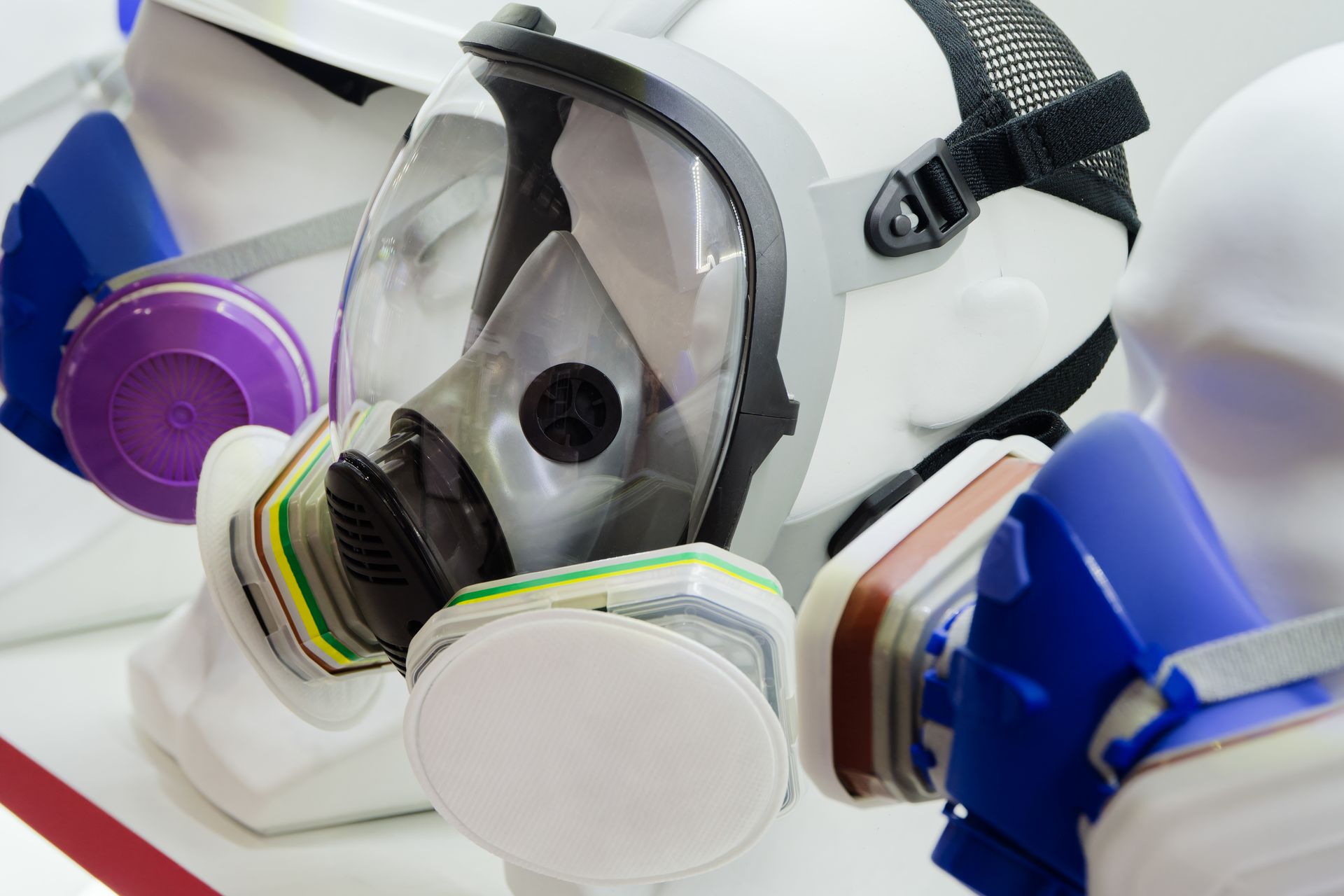White gas mask with clear visor and colorful filters on a white surface
