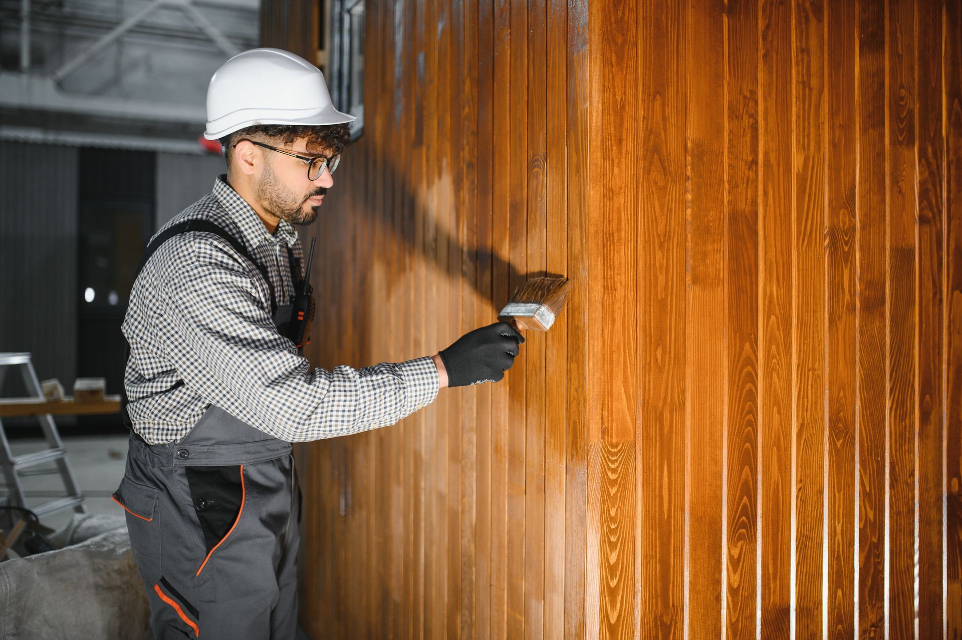Worker in hard hat spray-painting a wooden wall with a handheld sprayer.