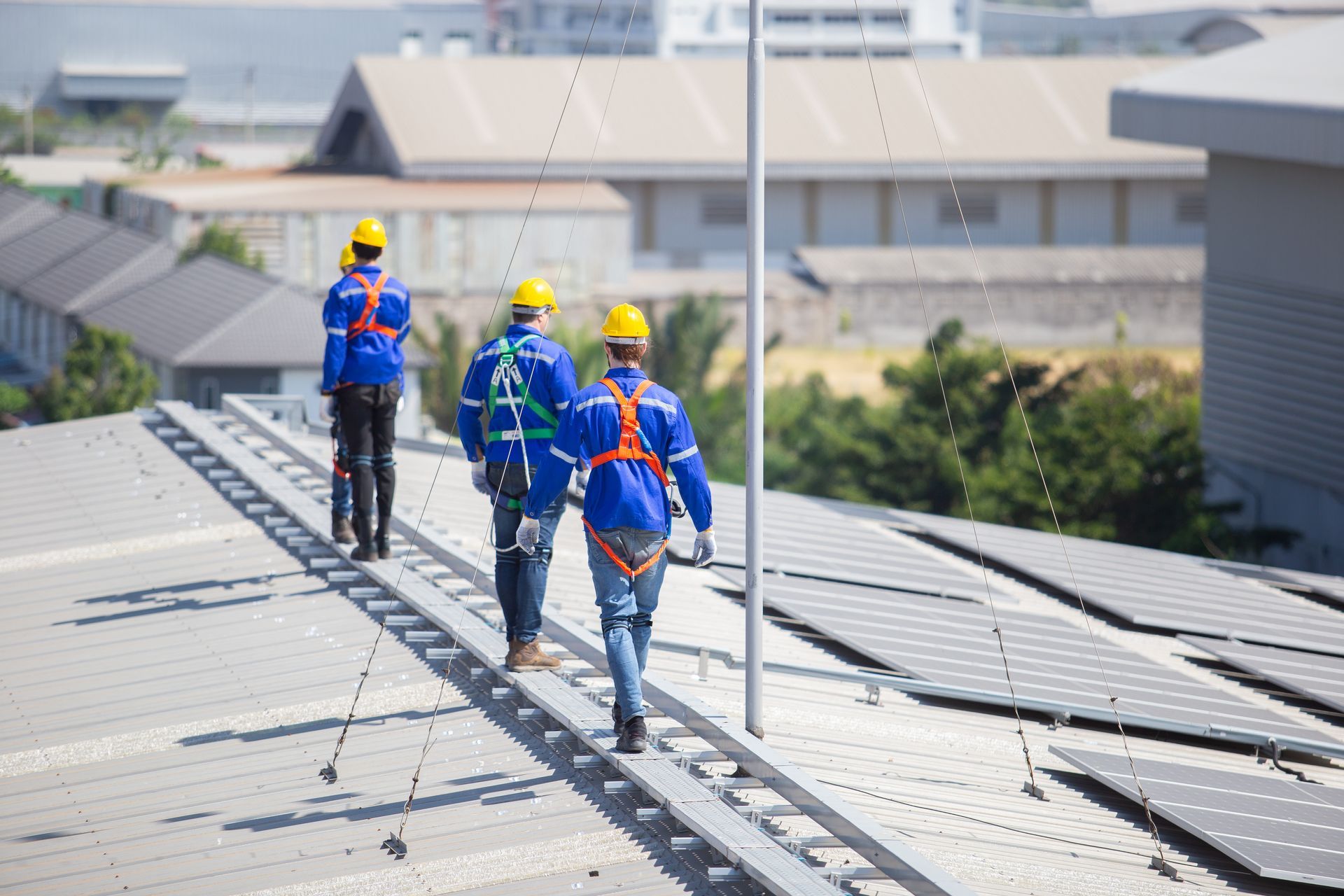 Four workers in safety gear walk along a rooftop walkway near solar panels.