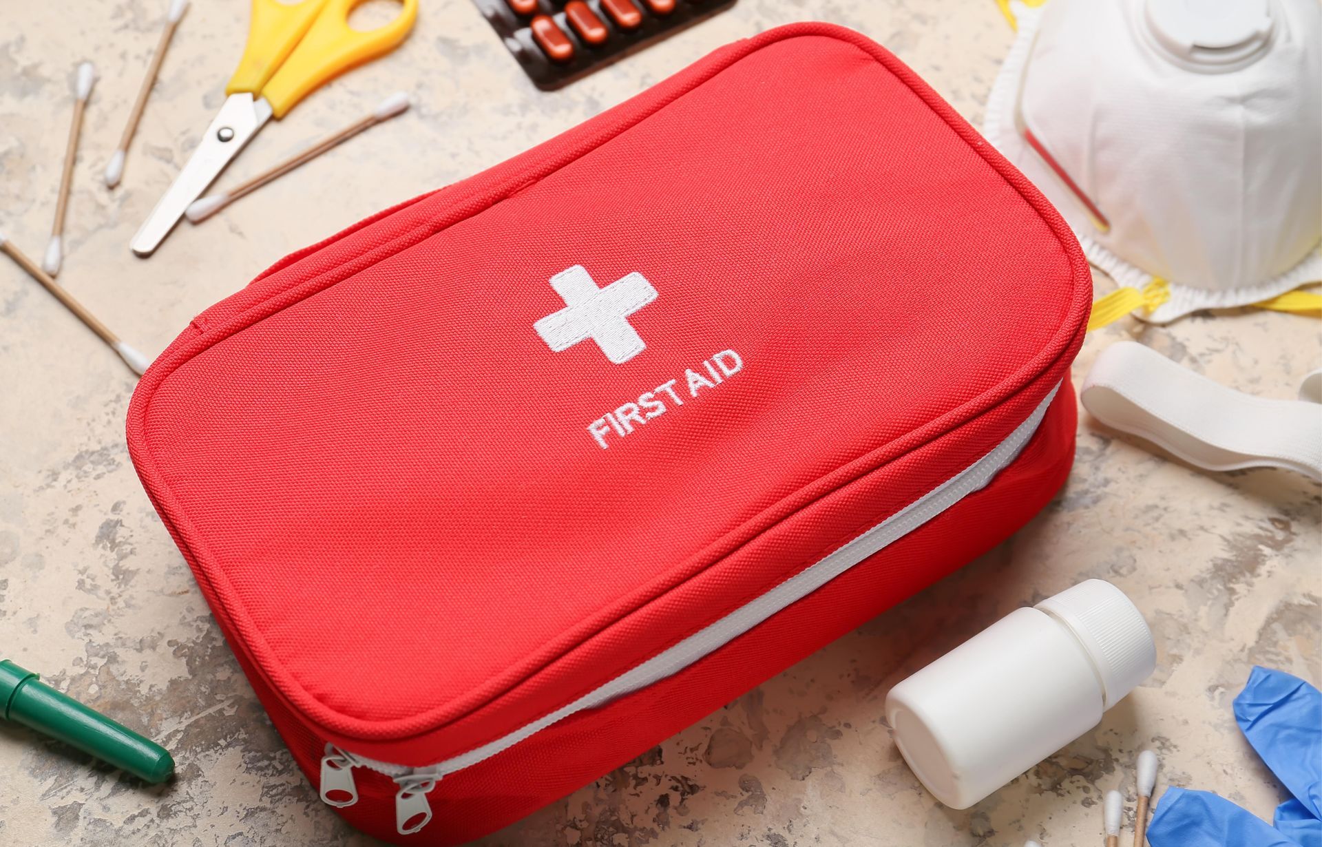 Red first aid kit with white cross on a tabletop, surrounded by scattered medical supplies.