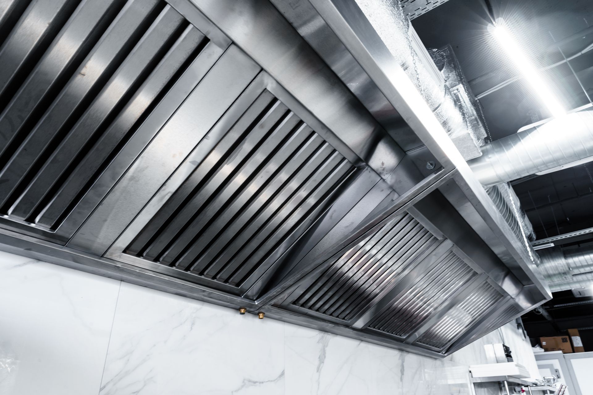 Stainless steel kitchen exhaust hoods and ventilation ducts overhead in an industrial kitchen