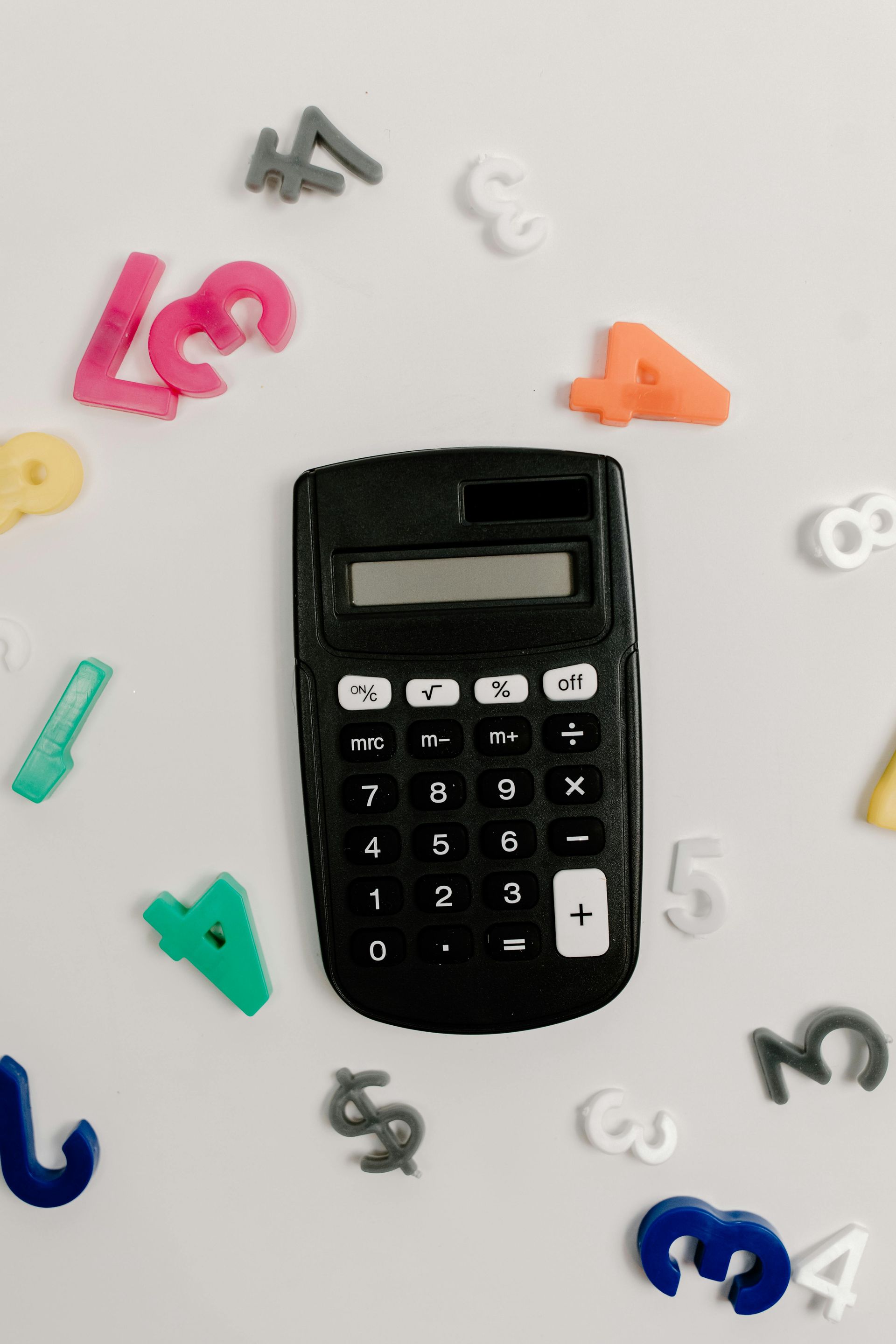 Black calculator centered among colorful scattered number magnets on a light background