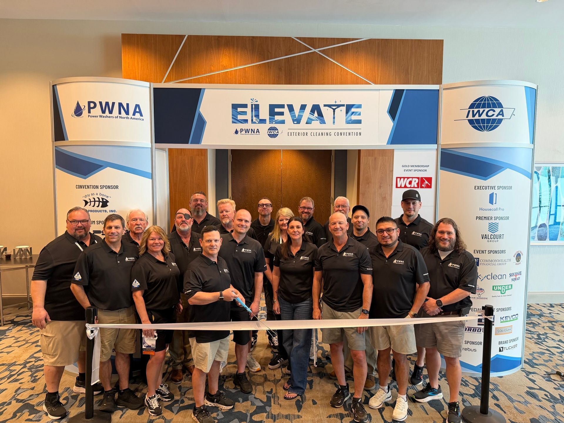 Group of people in black shirts posing at a branded ELEVATE event booth with a rope barrier