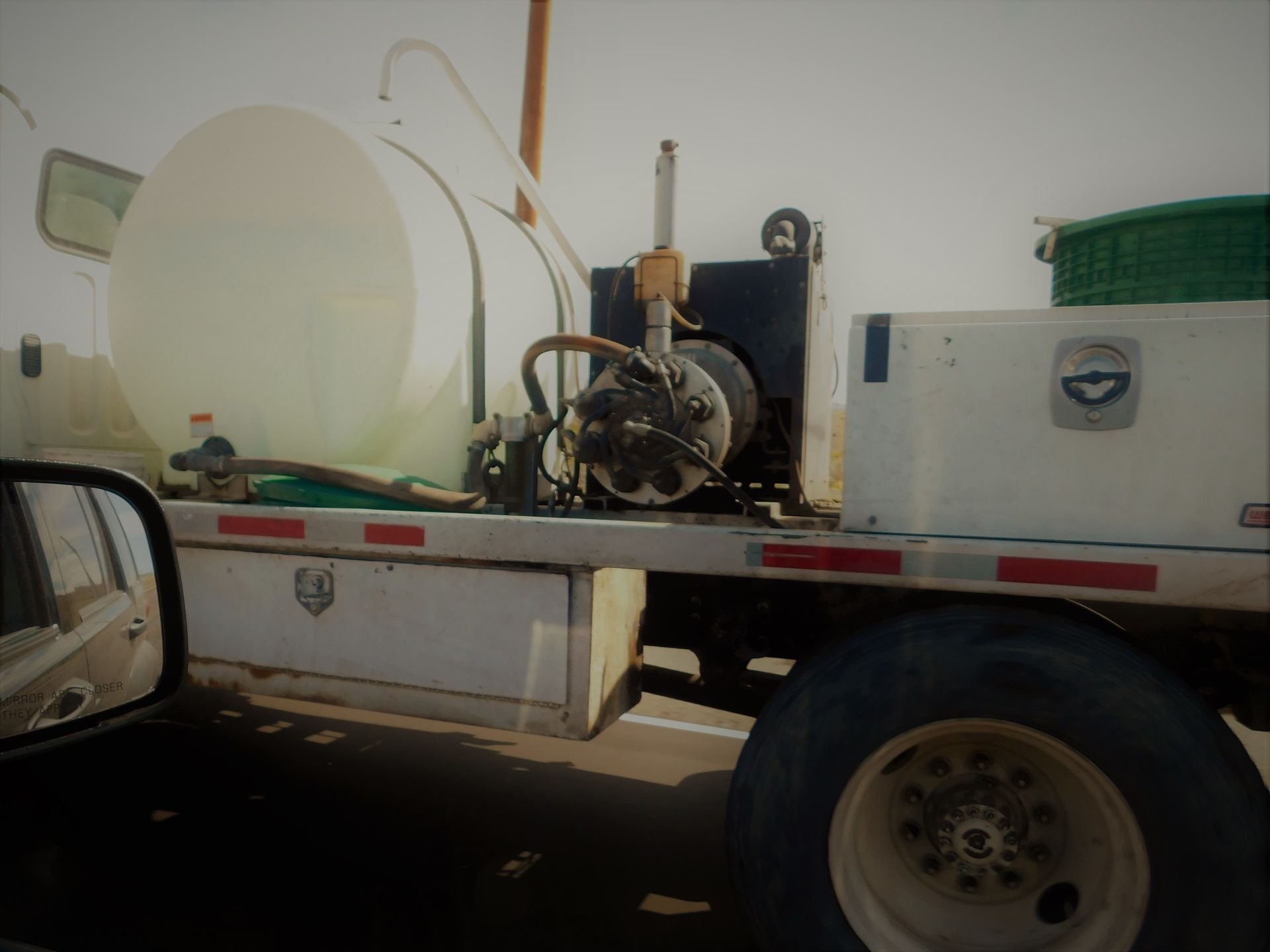 White utility trailer with equipment tanks and machinery, viewed from a vehicle beside it