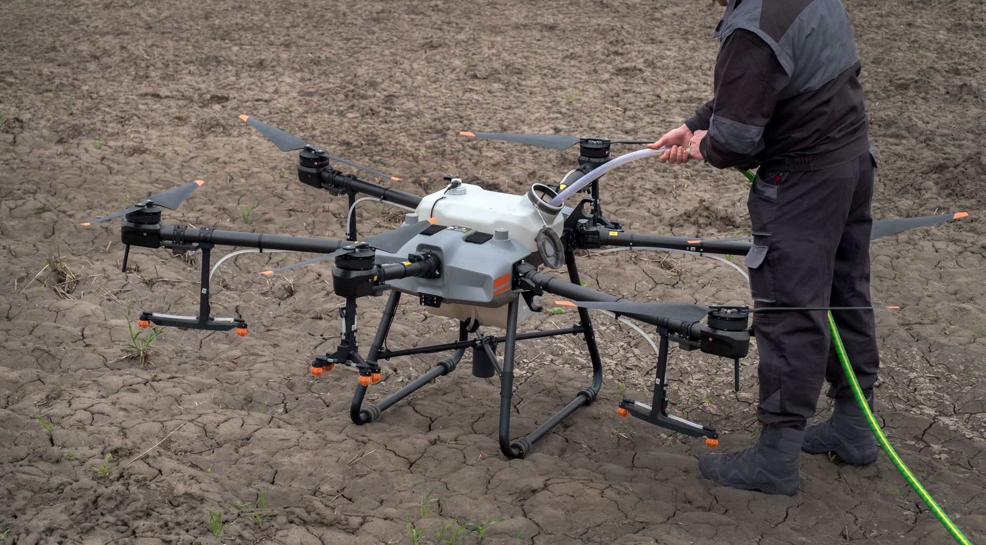 Person beside a large multirotor drone spraying liquid on a dirt field