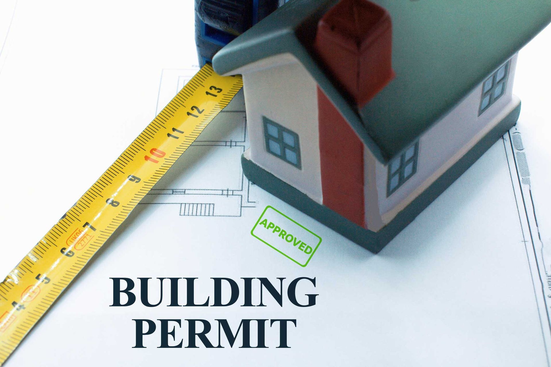 Toy house on a building permit with measuring tape, stamped