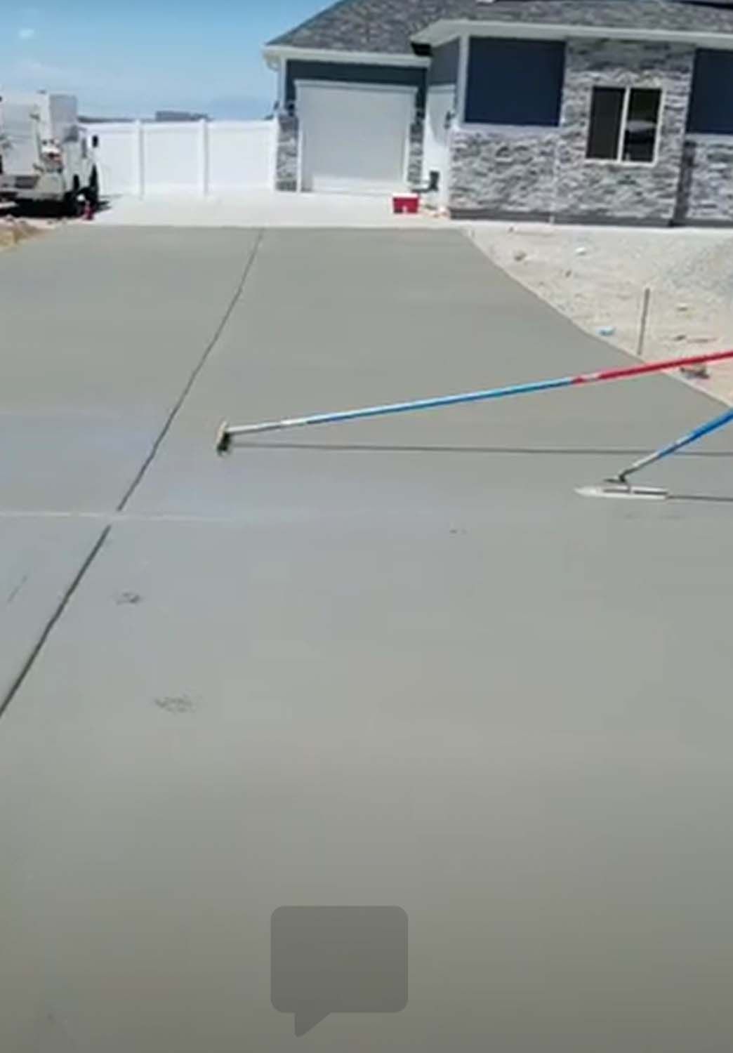 A person is spreading concrete on a driveway in front of a house.