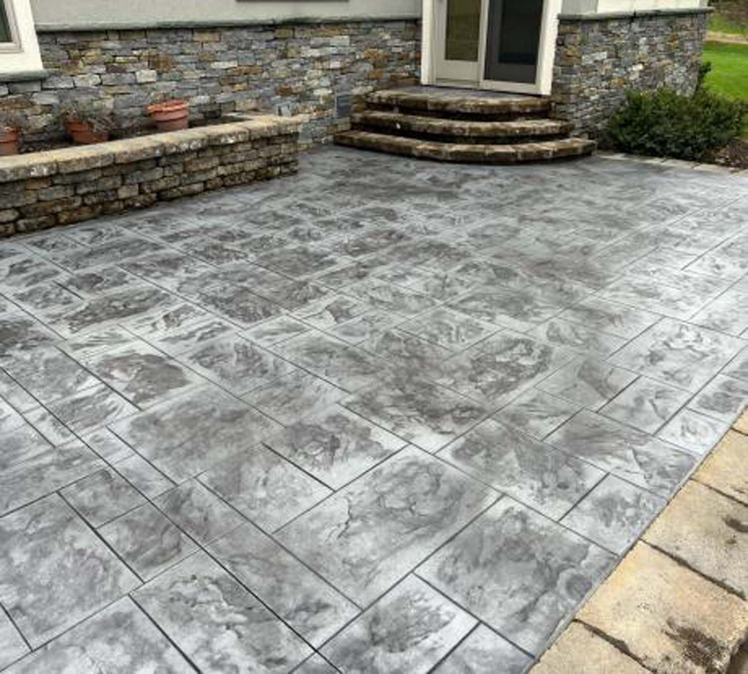 A concrete patio with stairs and a stone wall in front of a house.