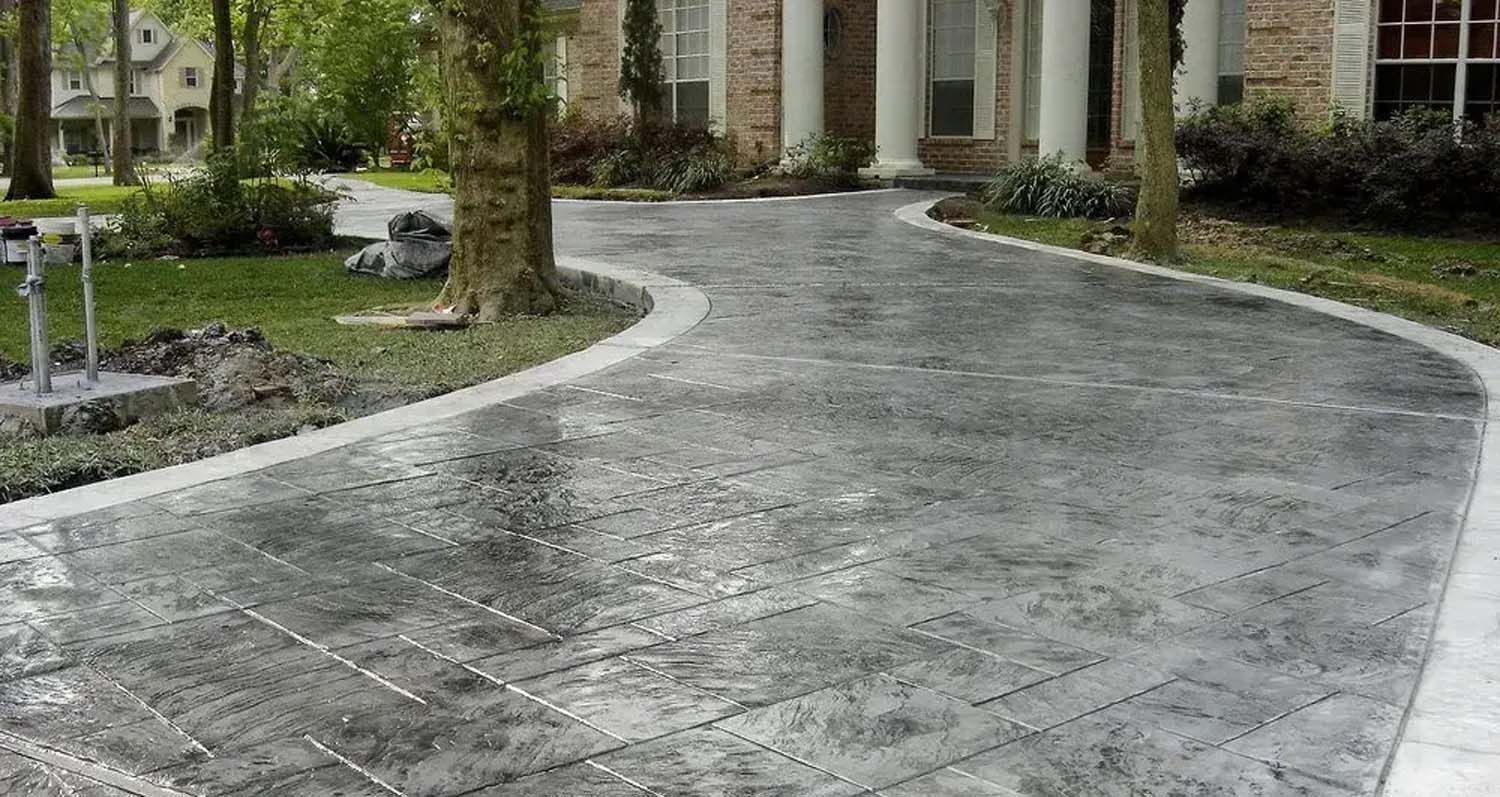 A concrete driveway leading to a house with trees in the background.