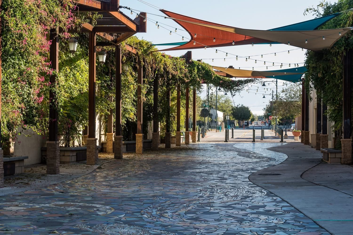 A stone walkway with a pergola and umbrellas in a park.