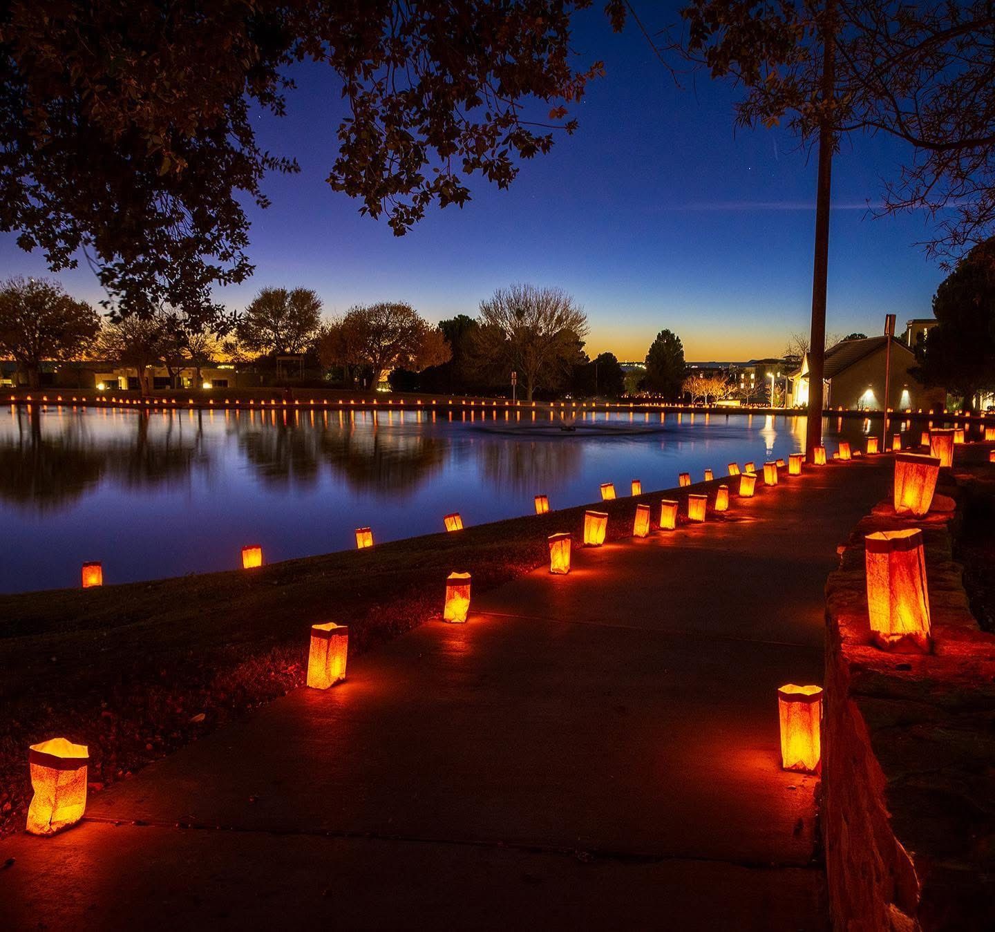 A row of paper lanterns are lit up on a sidewalk near a lake