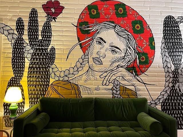 A mural of a woman wearing a sombrero is on a brick wall next to a green couch.