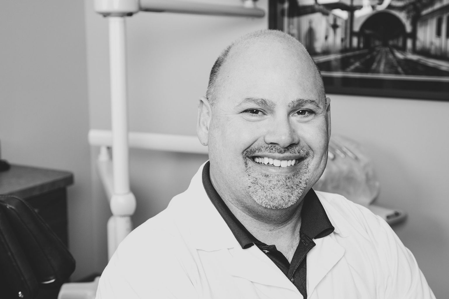 About Mike Ankermiller Smiling man in a white lab coat seated indoors, with medical equipment in the background