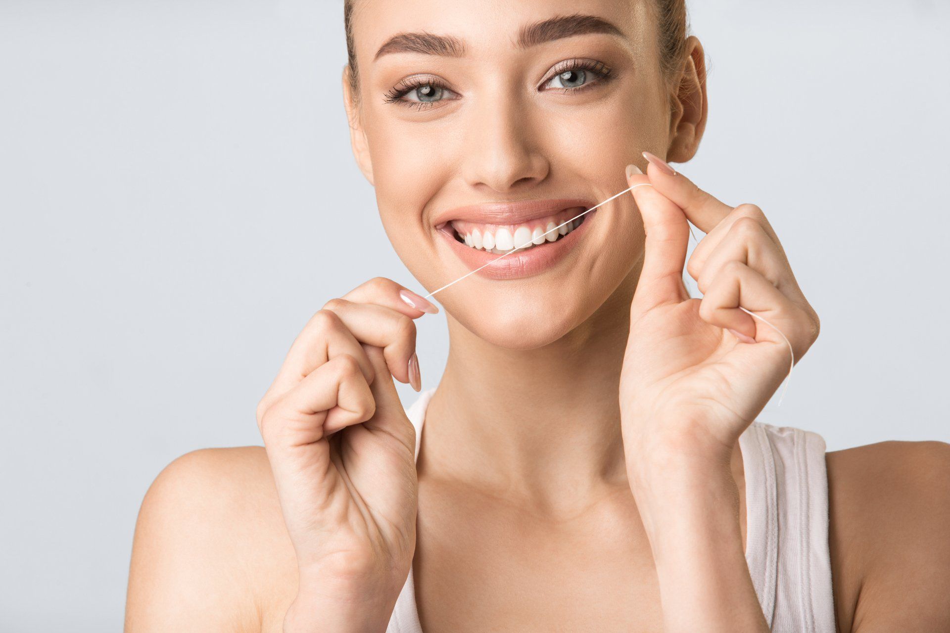 Smiling woman flossing teeth with clear dental floss against a light background