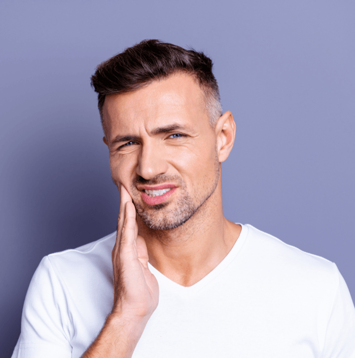 Man in white shirt touching his cheek against a plain blue background