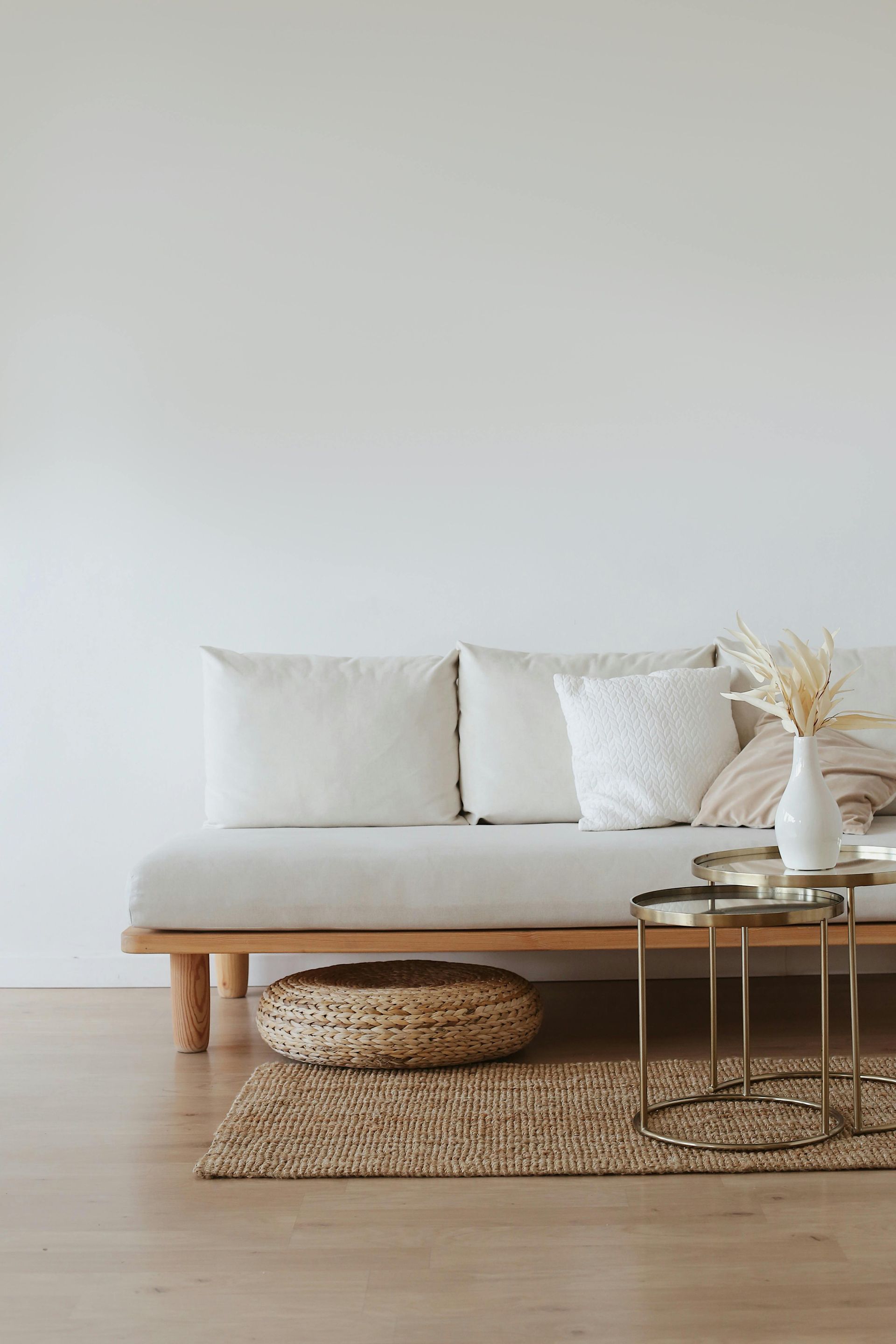 Beige couch with pillows, basket, rug, and gold side table against a white wall.