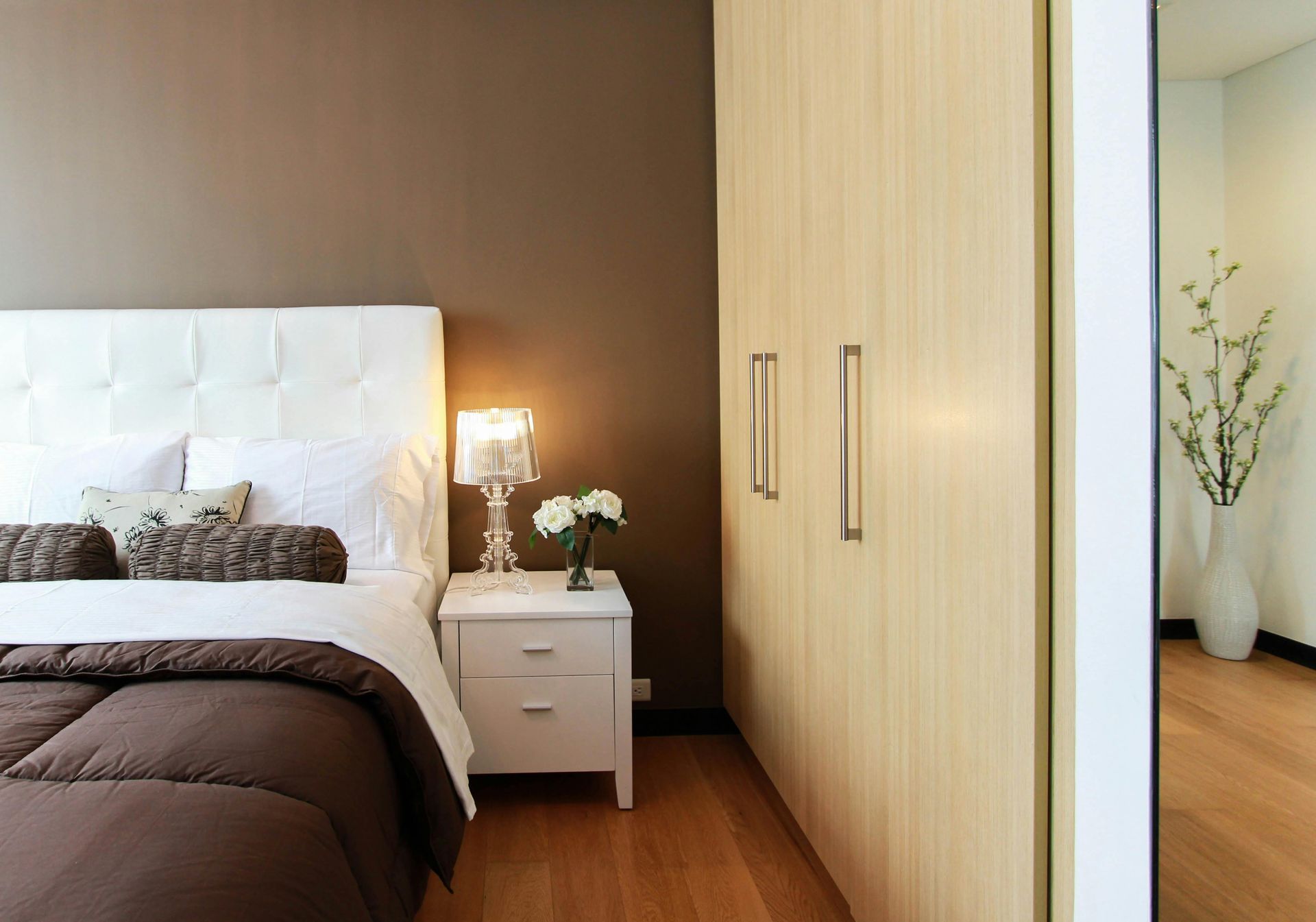 Bedroom with brown wall, white bed, nightstand with lamp, and a wood closet.