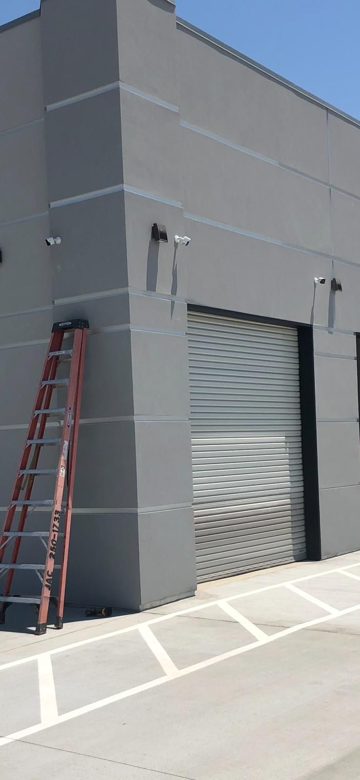 Gray industrial building with a closed roll-up door and a ladder leaning against the wall.