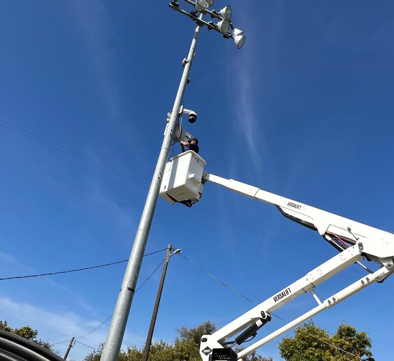 Utility worker in bucket lift repairing equipment on a tall pole against a blue sky