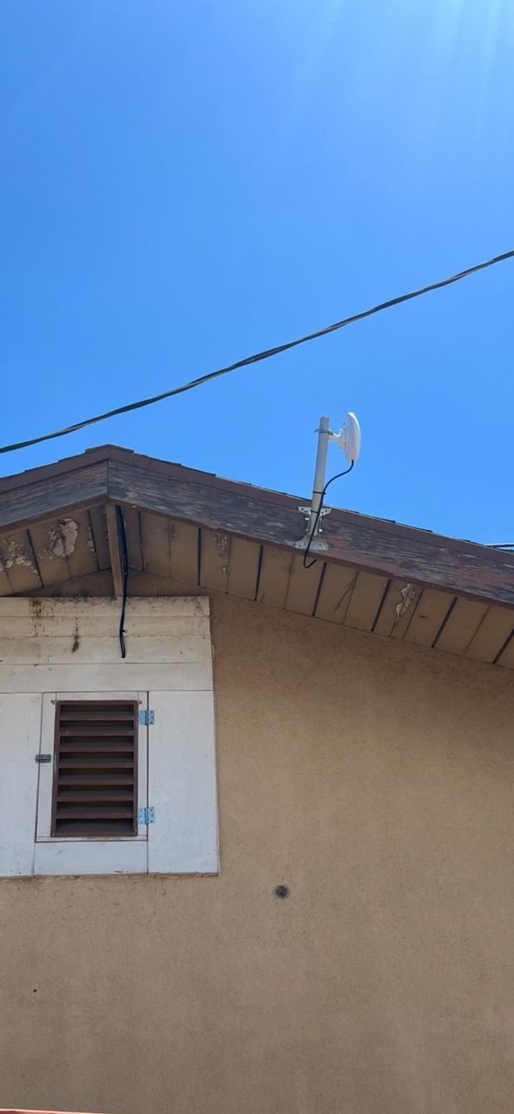 House exterior with beige wall, white window, roofline, and a satellite dish against a blue sky