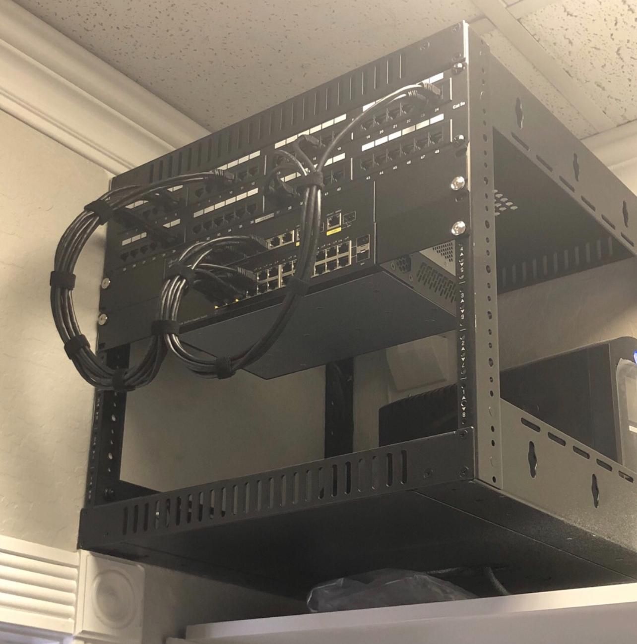 Black wall-mounted equipment rack with cables in a ceiling corner