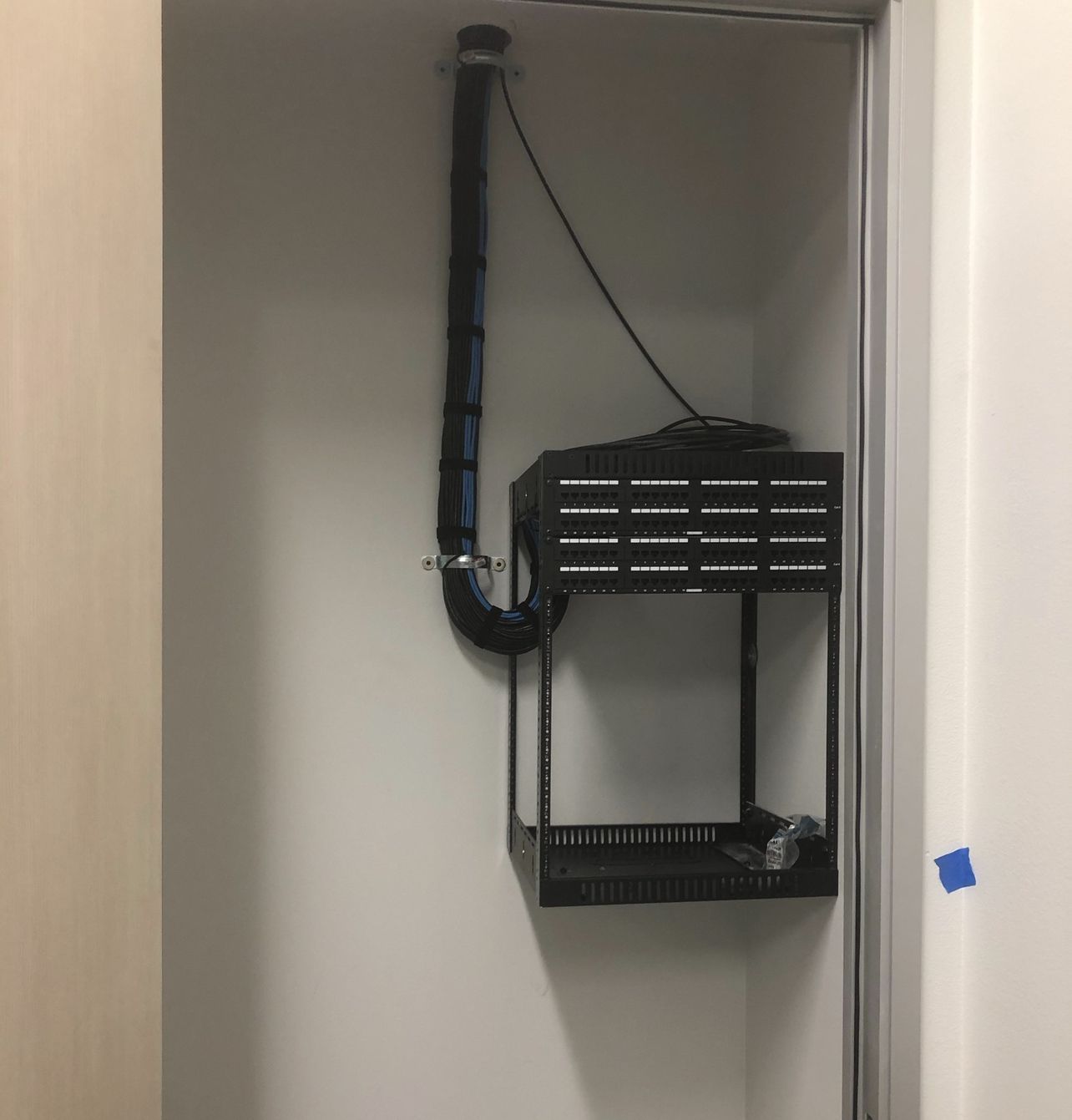Wall-mounted black equipment rack and cables inside a small closet or utility cabinet.