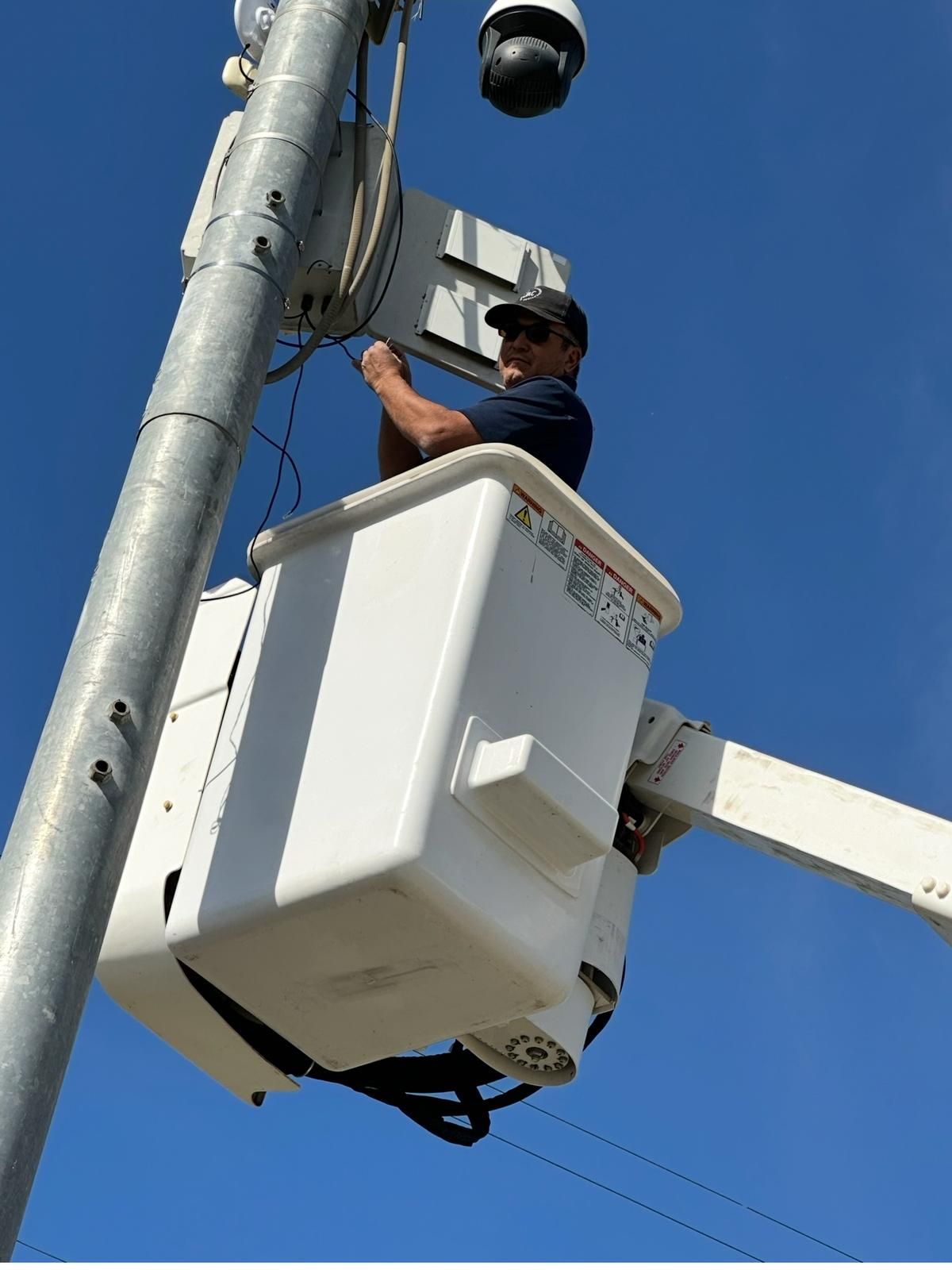 Worker servicing a traffic camera in a bucket lift against a blue sky