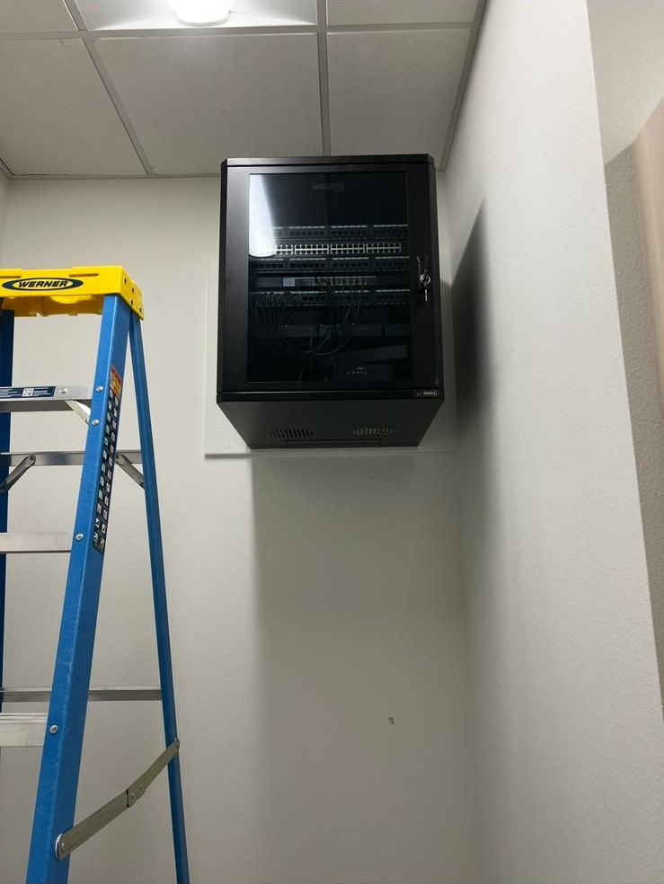 Blue ladder beside a black wall-mounted unit in a white room with ceiling tiles