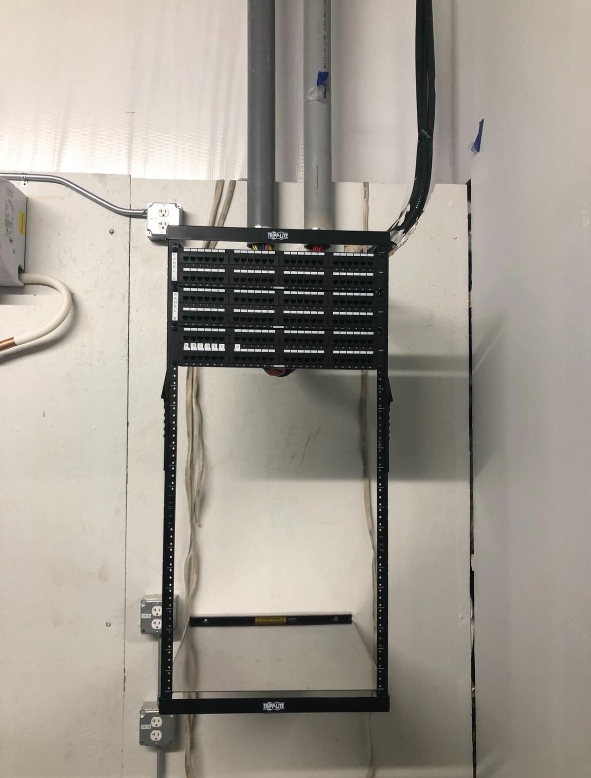 Black metal wall-mounted rack with cables and a lower rectangular frame in a utility room