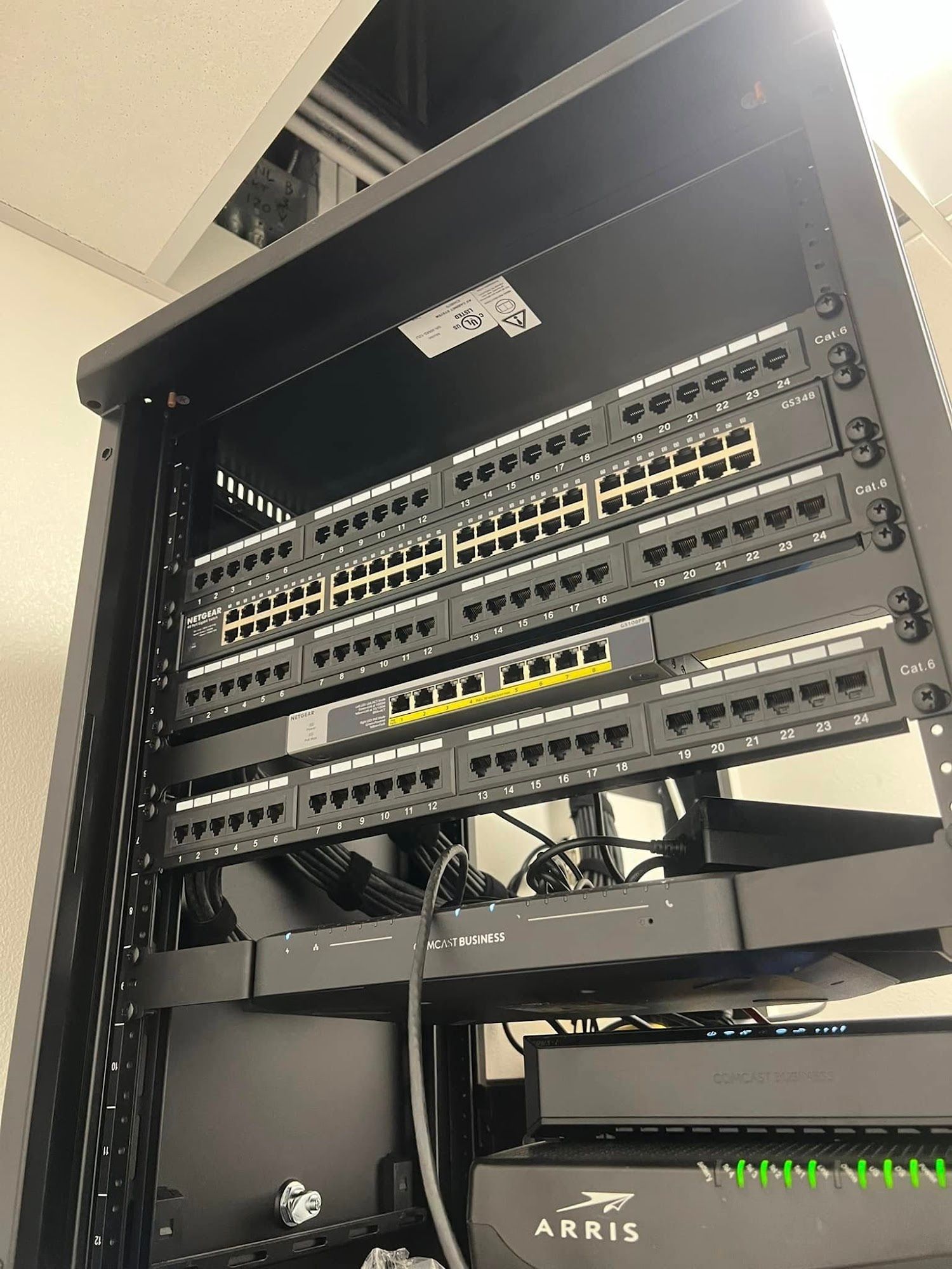 Network equipment rack with several mounted switches and routers, cables, and green status lights in a server closet