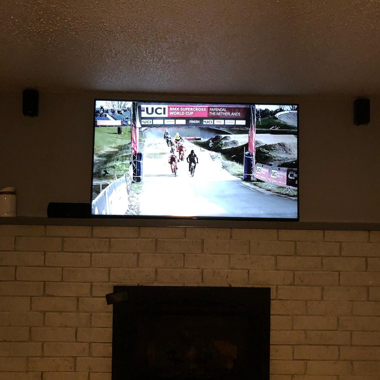 TV in a living room showing cyclists racing under a UCI finish banner above a fireplace