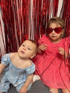Two little girls wearing heart shaped sunglasses are sitting next to each other.