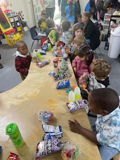 A group of children are sitting at a long table eating snacks.