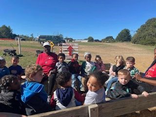 A group of children are sitting in a hay truck at a pumpkin patch.