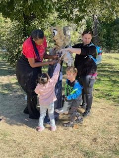 A group of people are standing around a mascot in a park.