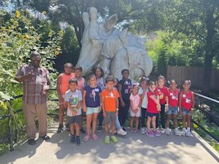 A group of children are posing for a picture in front of a rhino statue.
