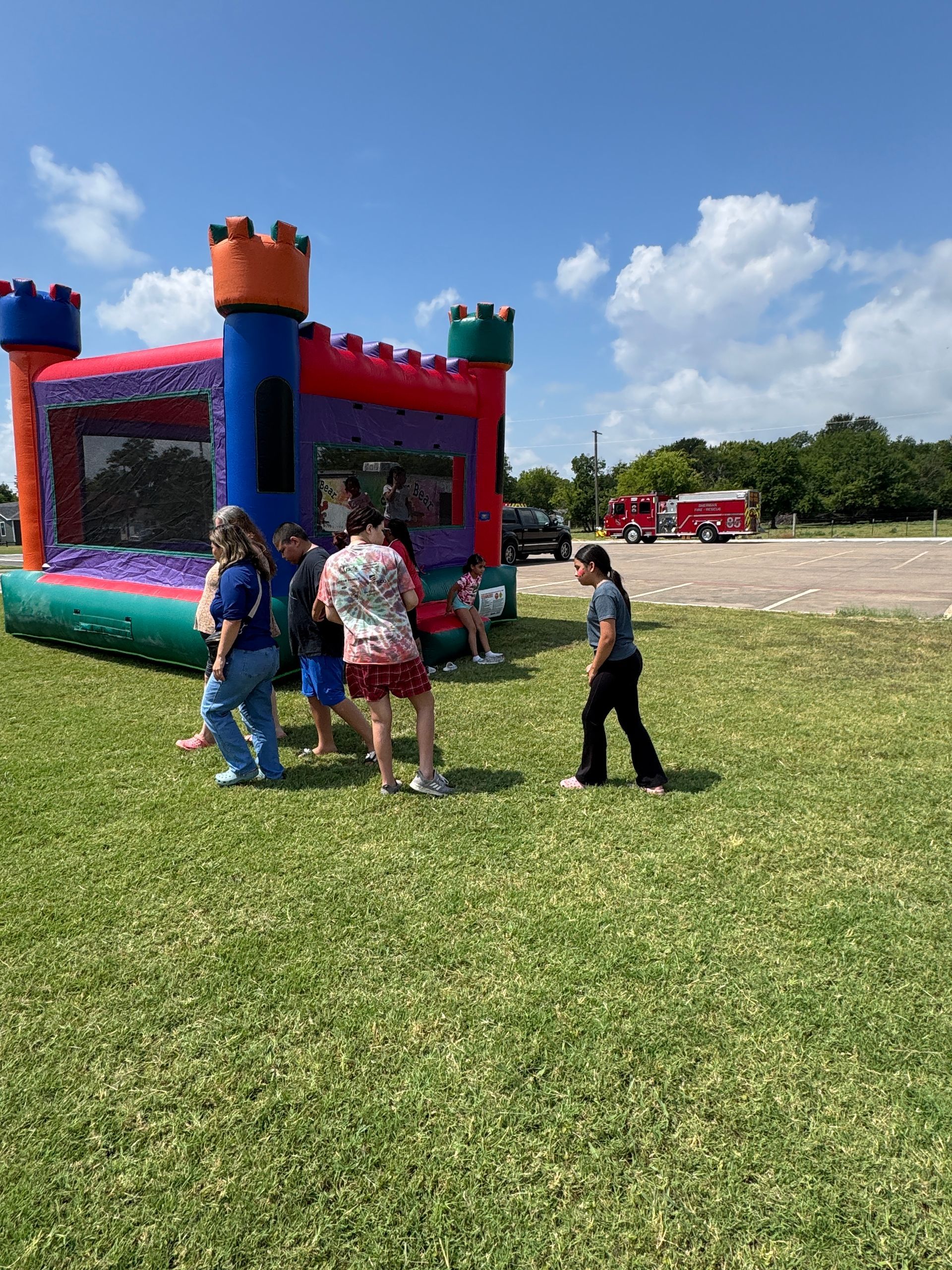 People stand near a colorful inflatable castle on a grassy area under a blue sky.