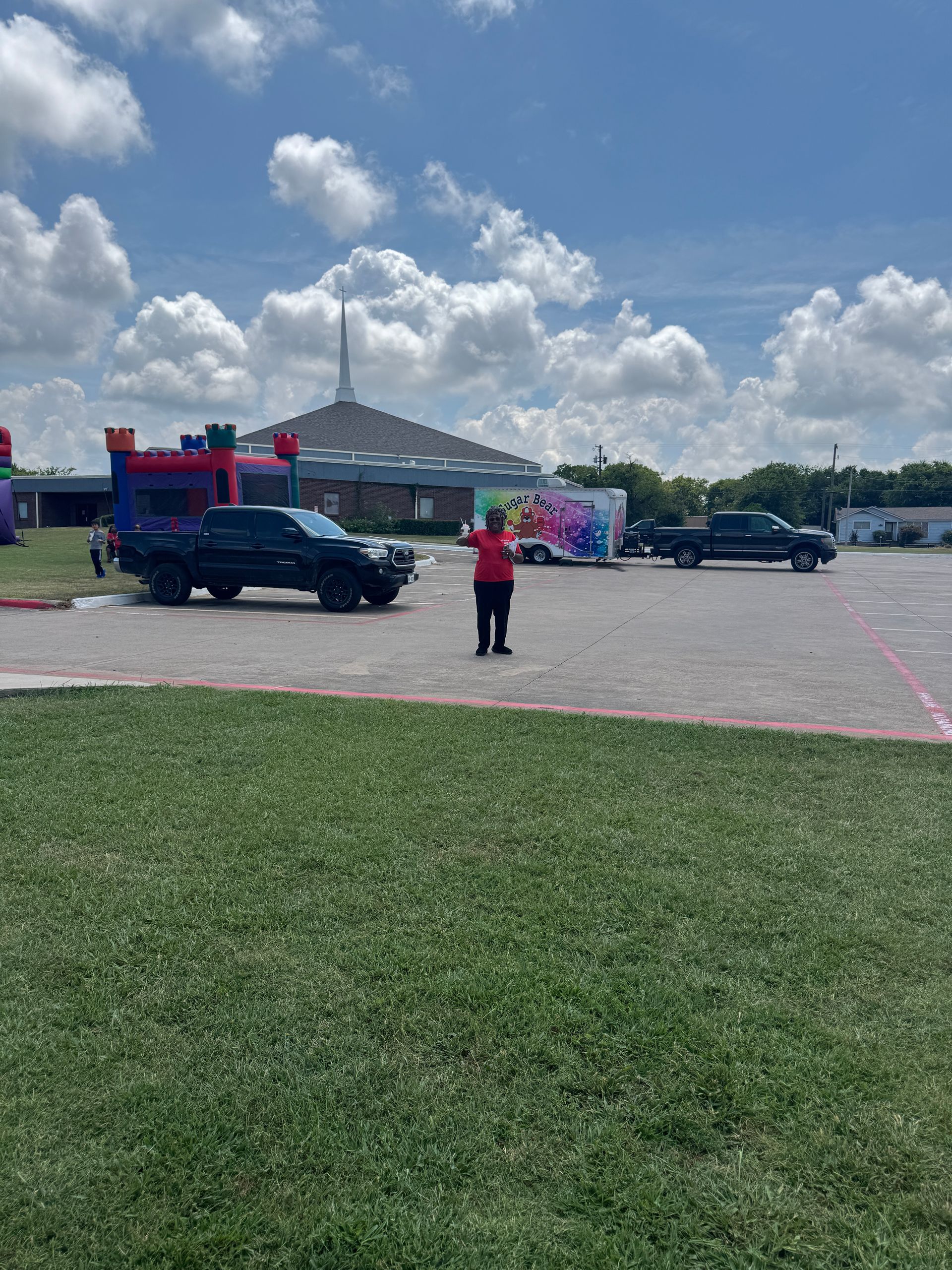 Person directing traffic on a bright day near a church with trucks and a bounce house.