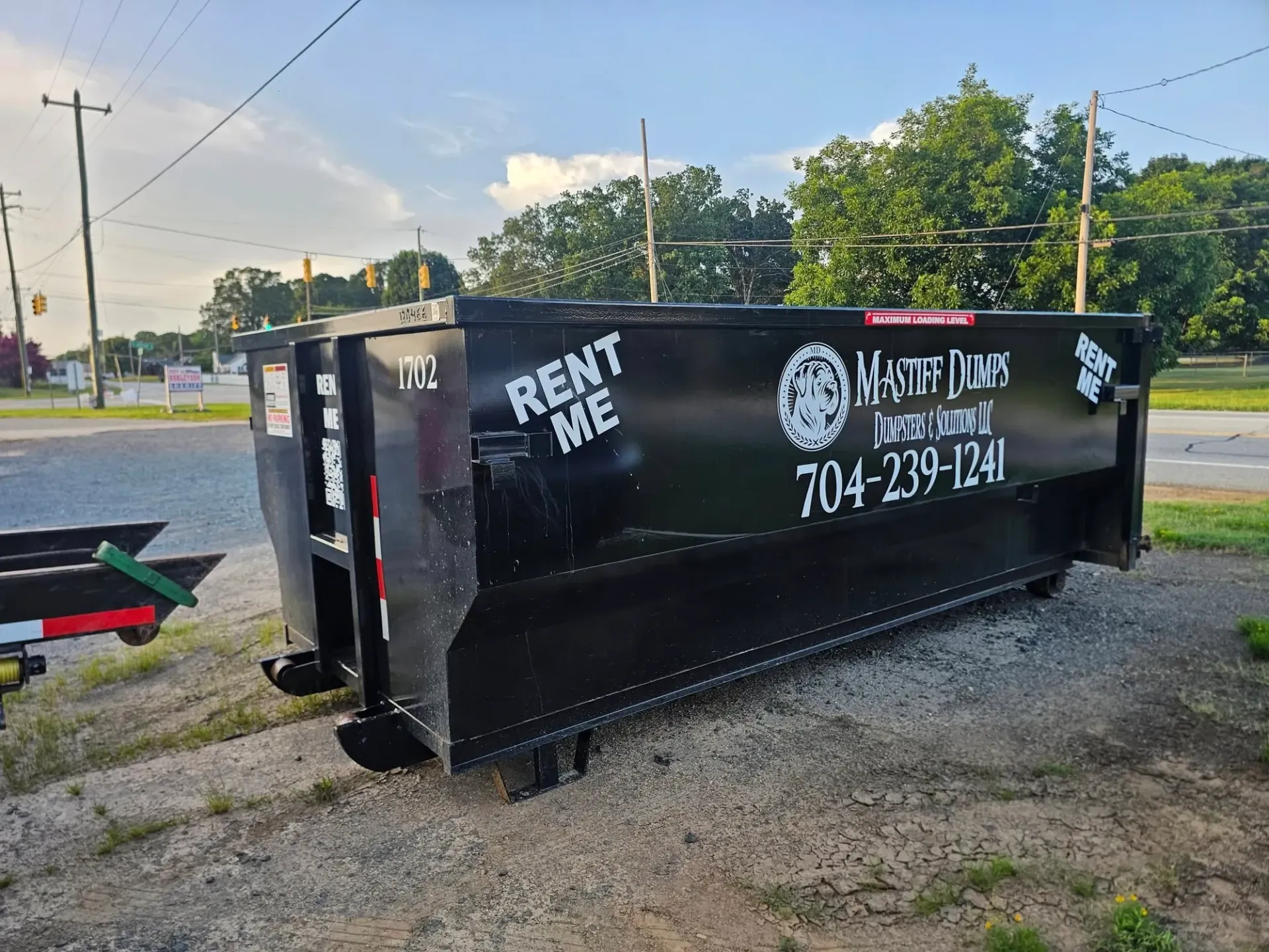 A black dumpster is sitting in front of a house under construction.