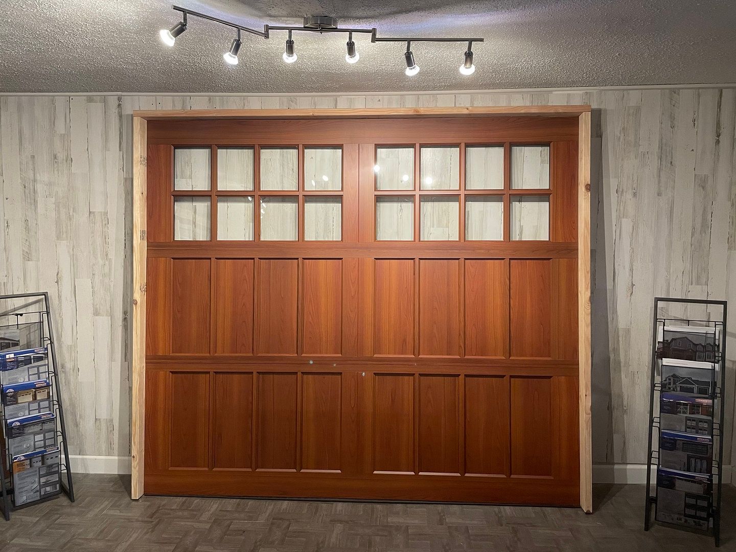 Wooden double doors with frosted windows in a gray wall, lit by track lights, with metal display racks on both sides