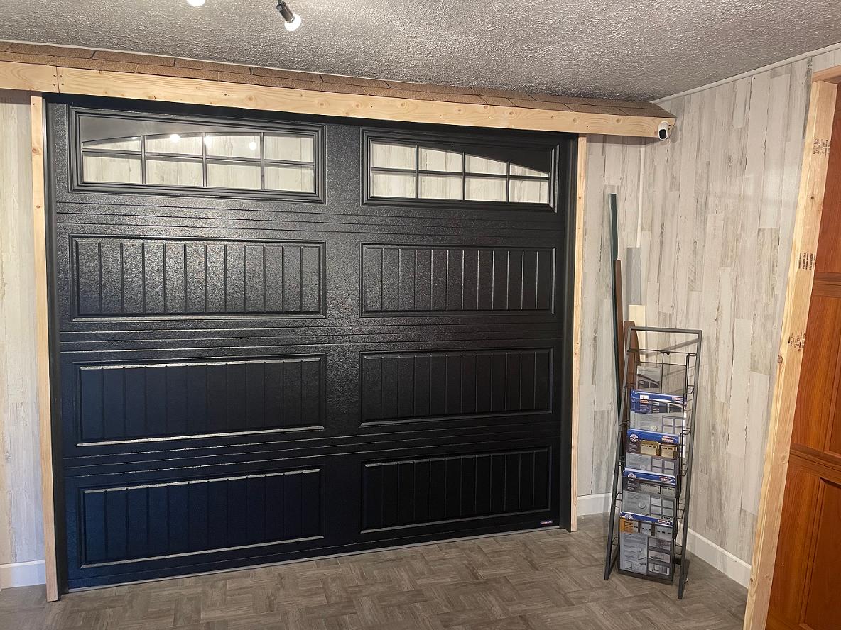 Black garage door with window panes inside a basement or garage room, beside a wire shelf and wood paneling