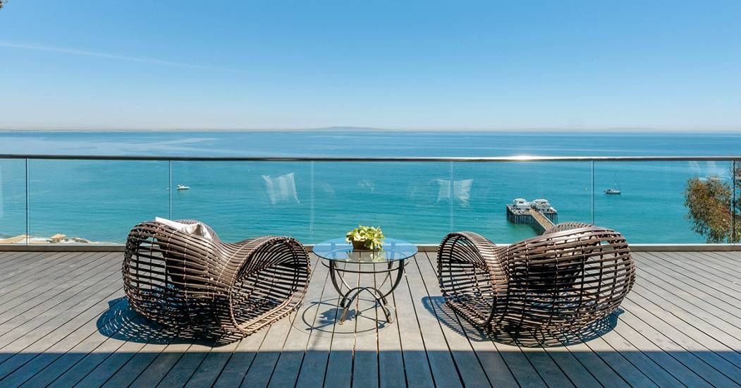 Two wicker lounge chairs on a seaside terrace overlooking a turquoise ocean