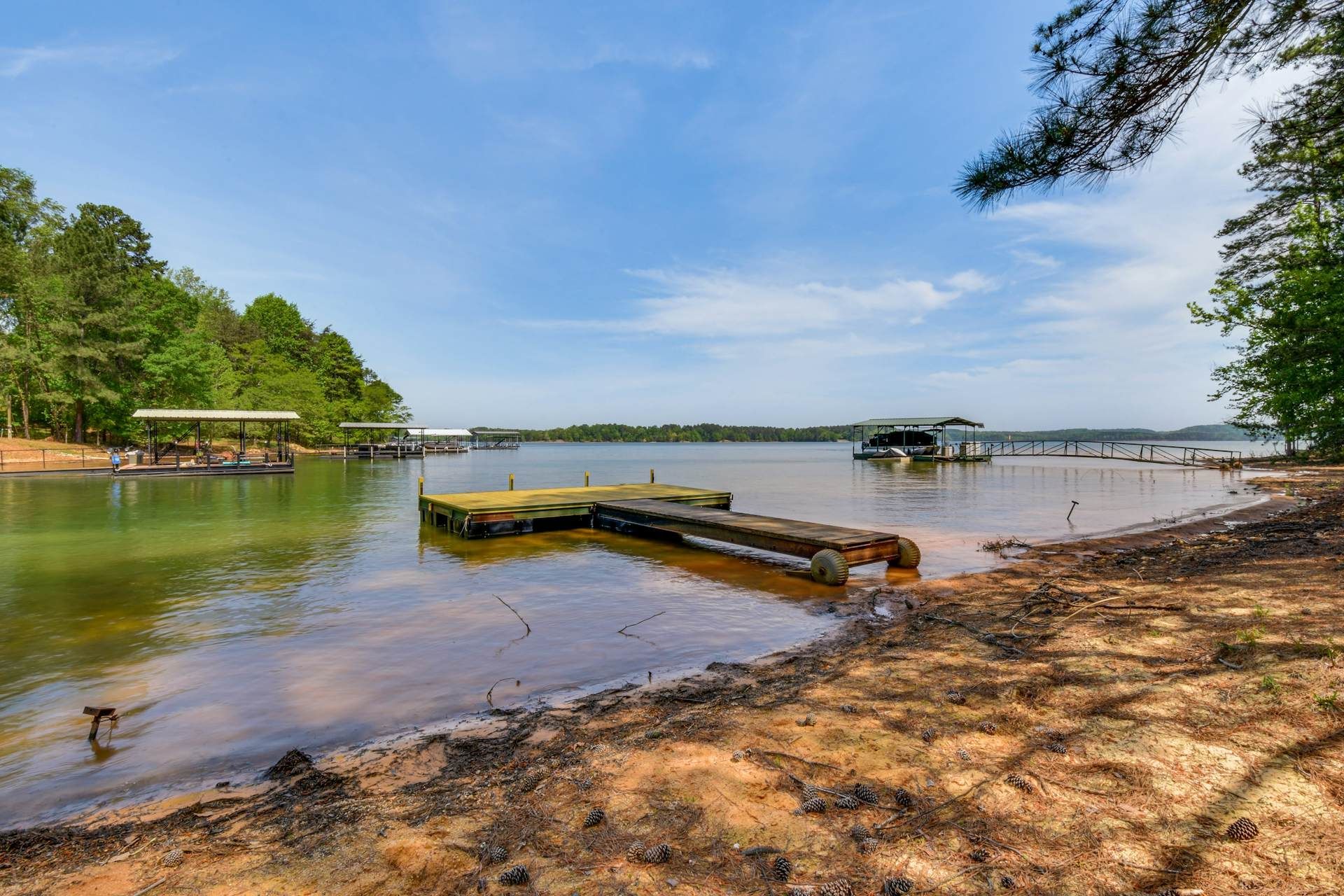 Sandy lakeshore with calm water, wooden dock, and trees under a clear blue sky