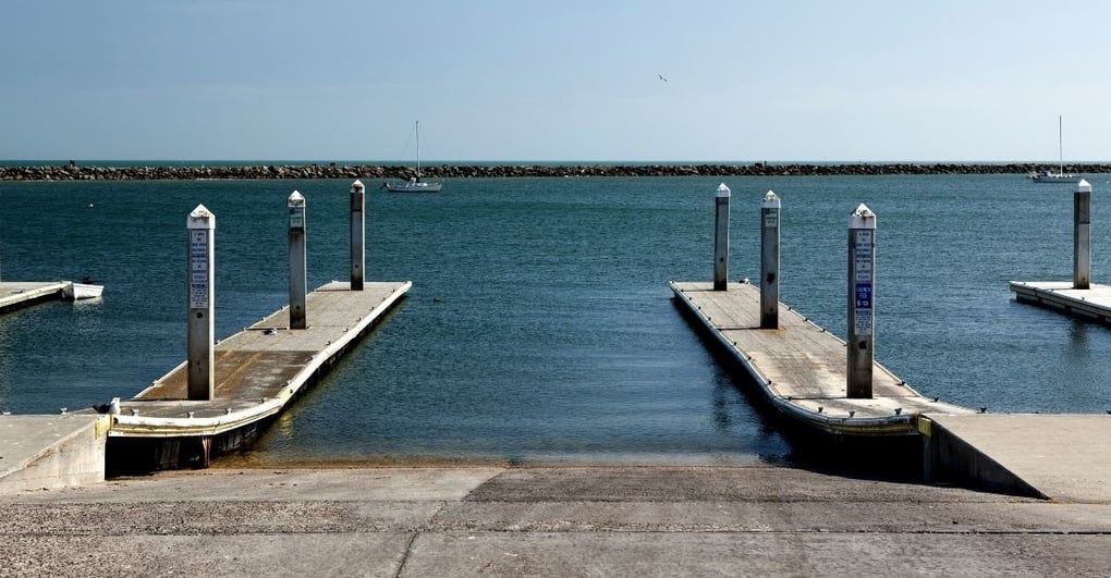 Concrete boat ramp with two docks extending into calm blue water under a clear sky