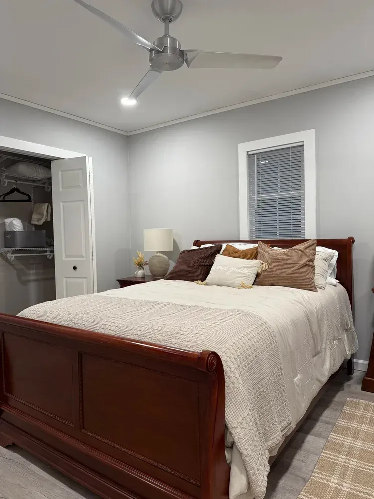 Bedroom with a dark wood bed, cream bedding, ceiling fan, bedside lamp, and open closet door.