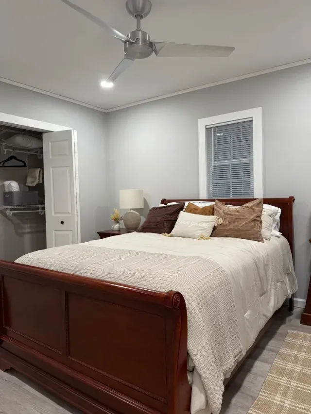 Bedroom with a wooden bed, cream bedding, gray walls, ceiling fan, and an open closet doorway.