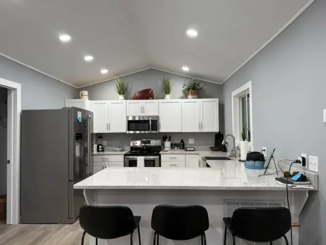 Modern gray kitchen with white island, black stools, stainless fridge, and recessed lighting